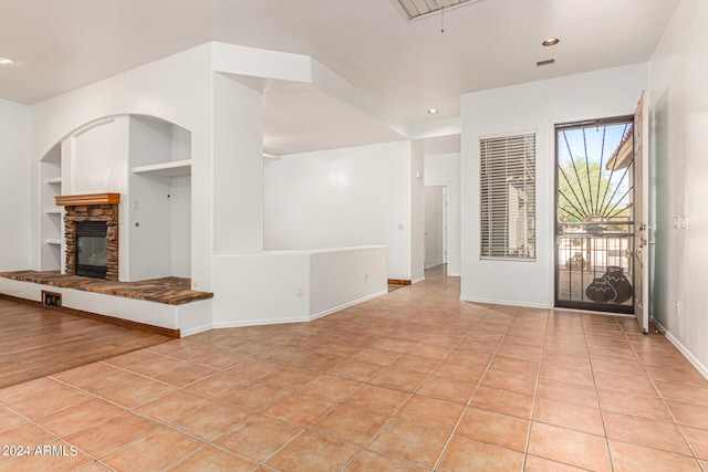 unfurnished living room featuring built in shelves, a stone fireplace, and light tile patterned floors