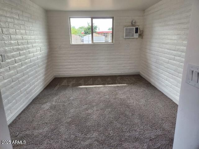 spare room with a wall mounted air conditioner, brick wall, and carpet flooring