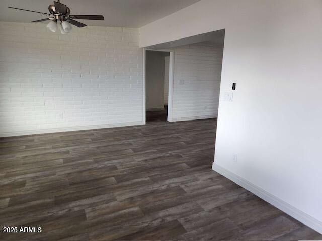 spare room featuring ceiling fan, brick wall, and dark hardwood / wood-style floors