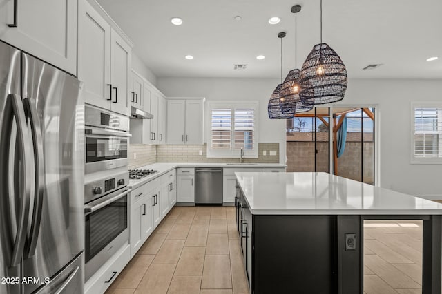 kitchen with under cabinet range hood, a sink, tasteful backsplash, appliances with stainless steel finishes, and light countertops