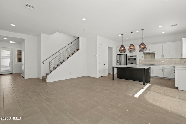 kitchen featuring visible vents, a kitchen island, light countertops, appliances with stainless steel finishes, and backsplash