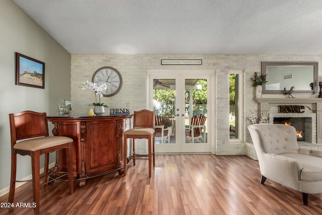 interior space with a textured ceiling, hardwood / wood-style floors, brick wall, and french doors