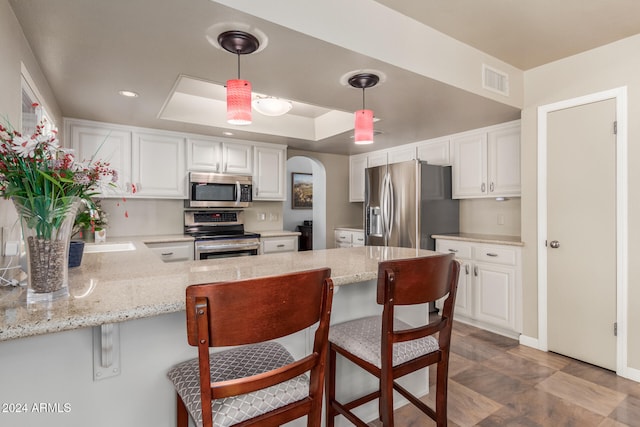 kitchen featuring kitchen peninsula, white cabinets, decorative light fixtures, and appliances with stainless steel finishes