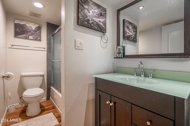 full bathroom featuring vanity, combined bath / shower with glass door, hardwood / wood-style flooring, and toilet