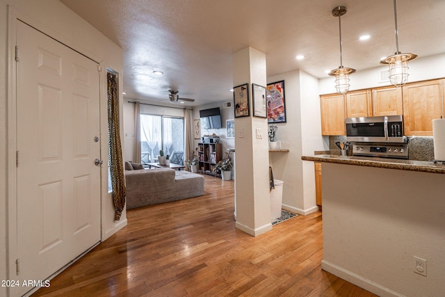 kitchen with appliances with stainless steel finishes, light brown cabinetry, ceiling fan, light hardwood / wood-style floors, and decorative light fixtures