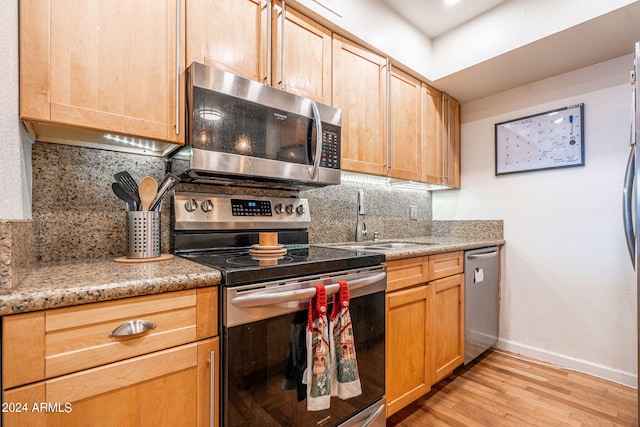 kitchen with light hardwood / wood-style flooring, stainless steel appliances, sink, light stone countertops, and tasteful backsplash