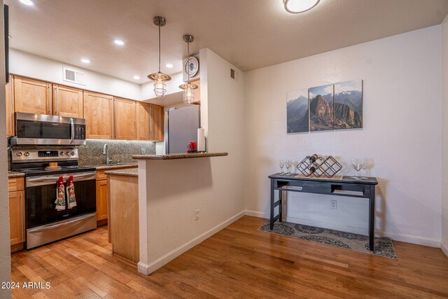 kitchen with tasteful backsplash, light stone countertops, appliances with stainless steel finishes, light wood-type flooring, and hanging light fixtures