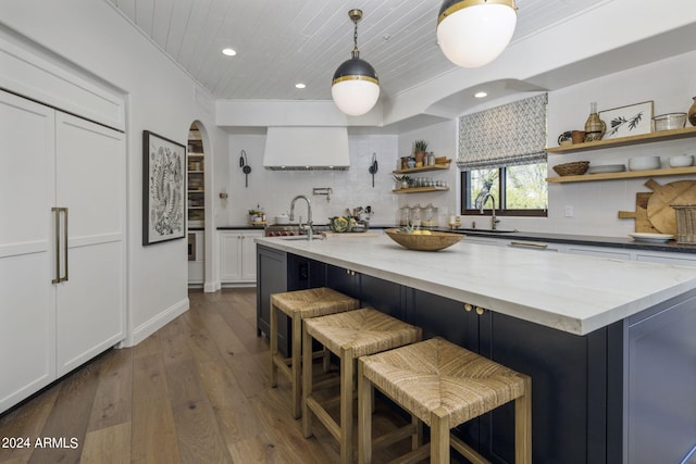 kitchen featuring dark wood-type flooring, tasteful backsplash, white cabinetry, a center island with sink, and dark stone countertops