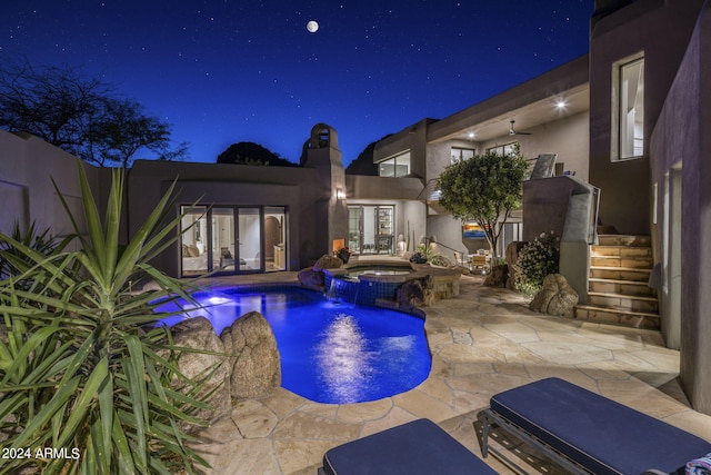 pool at night featuring a patio, an in ground hot tub, and pool water feature