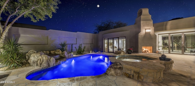 pool at twilight with a patio and an in ground hot tub