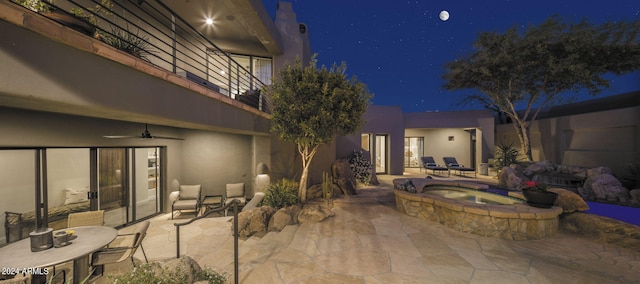 patio at night featuring a balcony and an in ground hot tub