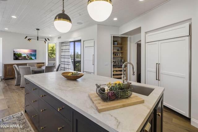 kitchen with light stone counters, pendant lighting, sink, dark wood-type flooring, and paneled fridge