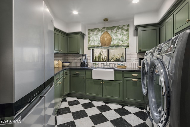 kitchen featuring sink, green cabinetry, backsplash, stainless steel refrigerator, and washing machine and dryer