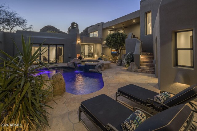 pool at dusk with a patio, an in ground hot tub, and pool water feature