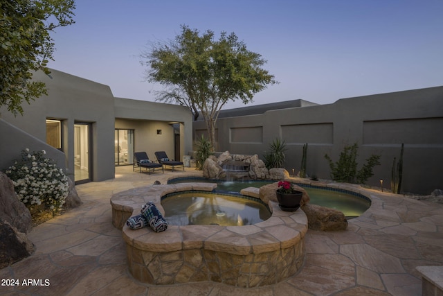 pool at dusk featuring pool water feature, a patio, and an in ground hot tub