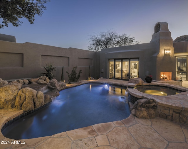 pool at dusk with a patio, an in ground hot tub, and pool water feature