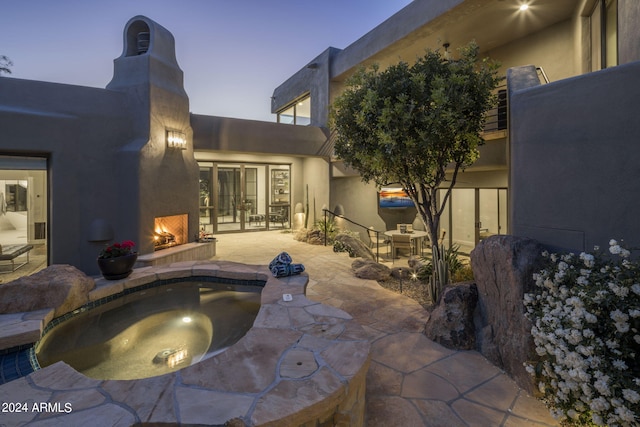 pool at dusk with exterior fireplace and a patio area