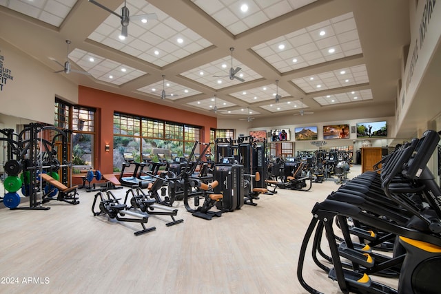 exercise room featuring light wood-type flooring, ceiling fan, coffered ceiling, and a high ceiling