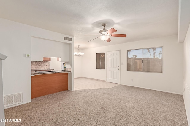 unfurnished living room featuring a textured ceiling, light carpet, and ceiling fan with notable chandelier