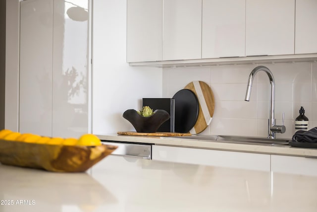 interior details with tasteful backsplash, sink, and white cabinets