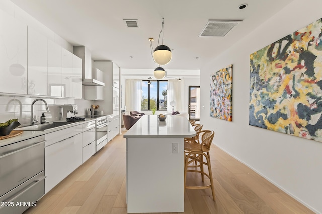 kitchen with a kitchen island, a breakfast bar, sink, white cabinets, and light hardwood / wood-style flooring