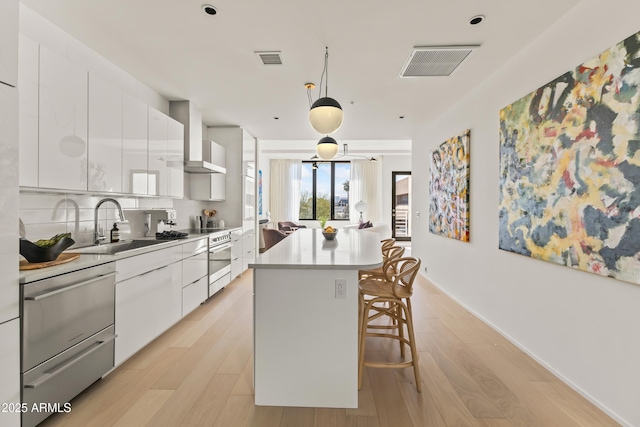 kitchen featuring sink, white cabinetry, a kitchen island, light hardwood / wood-style floors, and wall chimney range hood