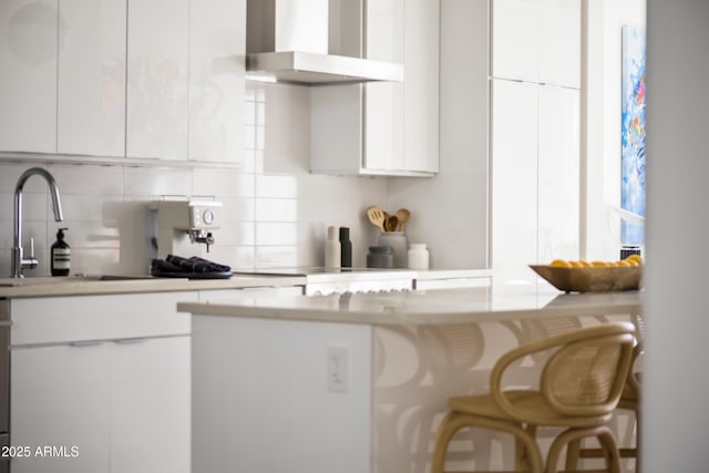 kitchen featuring tasteful backsplash, white cabinetry, sink, a breakfast bar area, and wall chimney exhaust hood