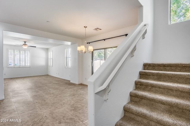 stairs featuring ceiling fan with notable chandelier