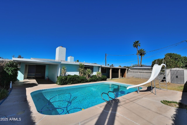 view of swimming pool with a fenced in pool, an outbuilding, a storage unit, a patio area, and a water slide