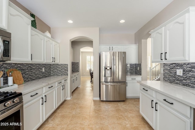 kitchen with light stone counters, appliances with stainless steel finishes, backsplash, and white cabinets