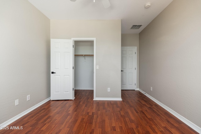 unfurnished bedroom featuring a closet, a spacious closet, dark hardwood / wood-style floors, and ceiling fan