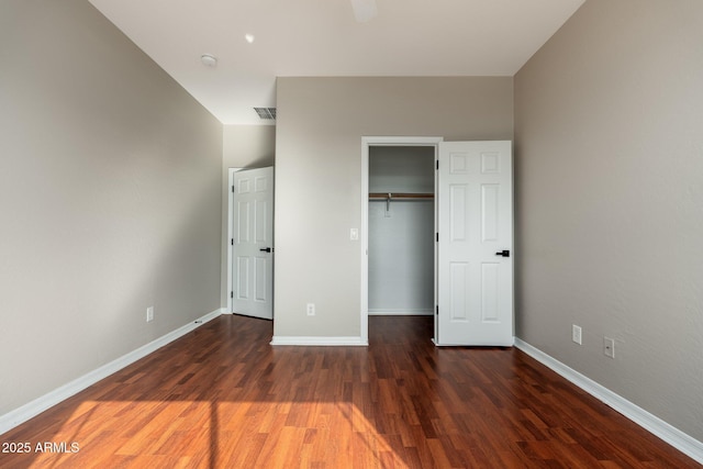 unfurnished bedroom with a spacious closet, dark wood-type flooring, and a closet