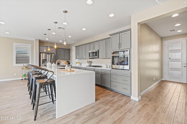 kitchen with hanging light fixtures, gray cabinetry, stainless steel appliances, and a kitchen island with sink