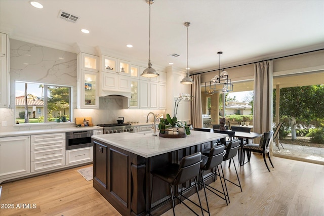 kitchen featuring tasteful backsplash, white cabinetry, a center island with sink, and light stone counters