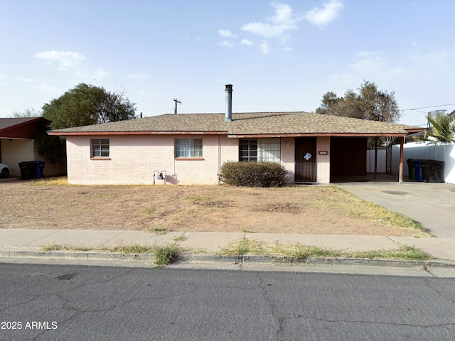 ranch-style home with an attached carport, brick siding, fence, concrete driveway, and roof with shingles