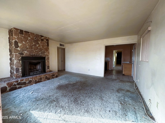 unfurnished living room with a stone fireplace, carpet, and visible vents