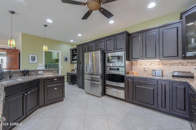 kitchen featuring appliances with stainless steel finishes, sink, dark brown cabinets, decorative light fixtures, and dark stone countertops