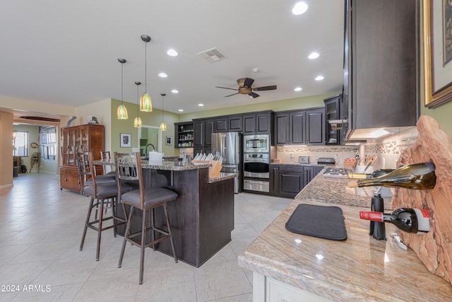 kitchen featuring hanging light fixtures, ceiling fan, appliances with stainless steel finishes, light stone countertops, and a center island