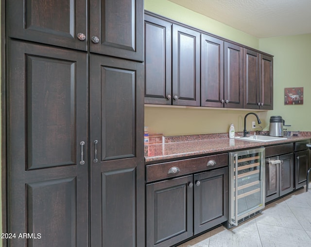 kitchen featuring a textured ceiling, dark brown cabinets, sink, and beverage cooler