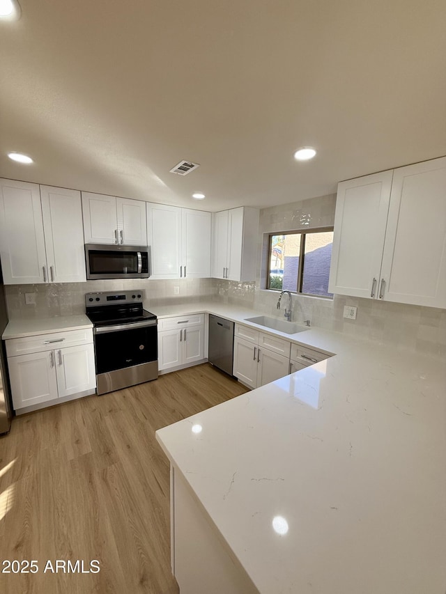 kitchen featuring white cabinetry, stainless steel appliances, sink, backsplash, and light hardwood / wood-style flooring