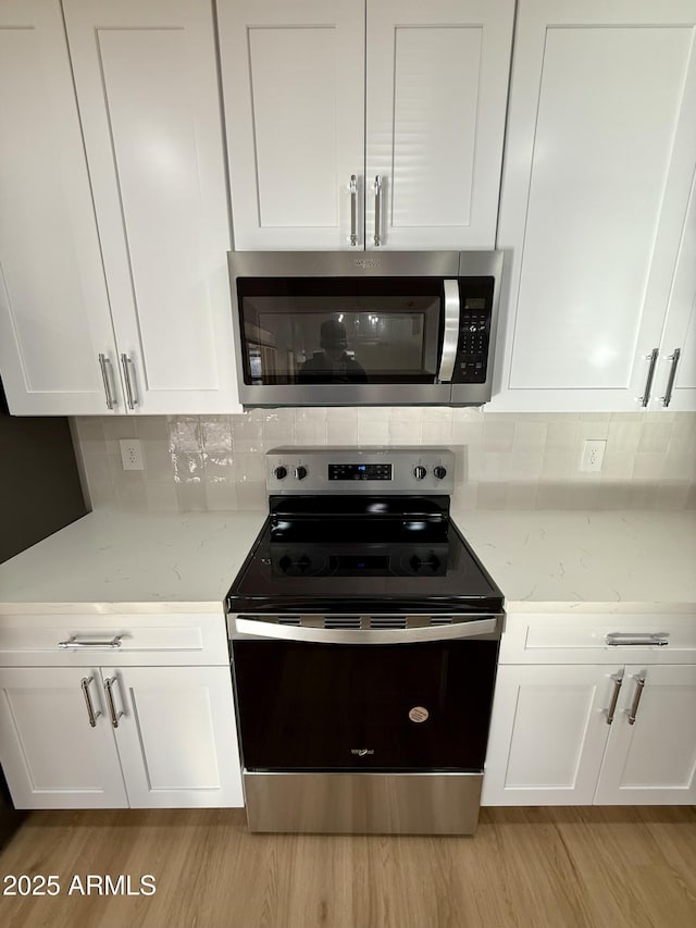 kitchen with tasteful backsplash, white cabinetry, light hardwood / wood-style flooring, light stone countertops, and appliances with stainless steel finishes