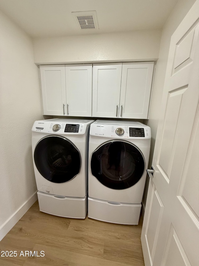 clothes washing area with washing machine and dryer, cabinets, and light wood-type flooring