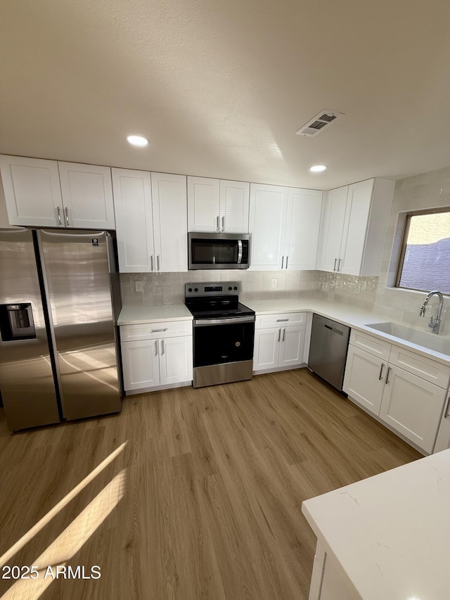 kitchen with light hardwood / wood-style floors, stainless steel appliances, backsplash, white cabinets, and sink