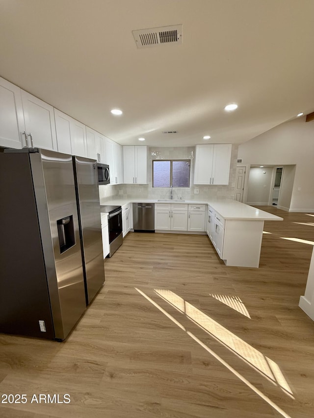 kitchen with backsplash, kitchen peninsula, sink, white cabinetry, and appliances with stainless steel finishes