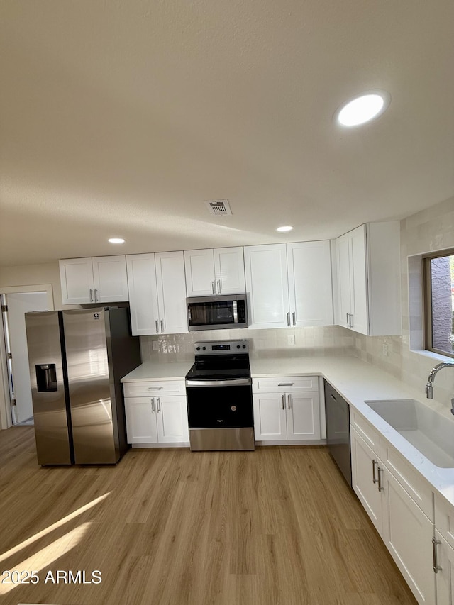 kitchen with light wood-type flooring, stainless steel appliances, white cabinets, and tasteful backsplash