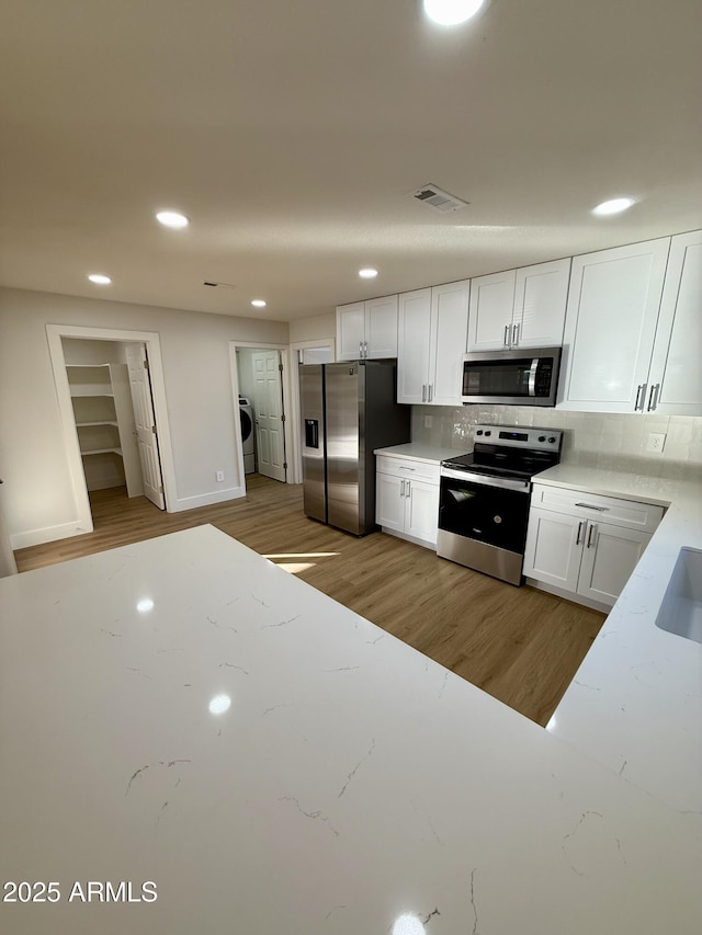 kitchen with washer / dryer, decorative backsplash, white cabinetry, light wood-type flooring, and stainless steel appliances