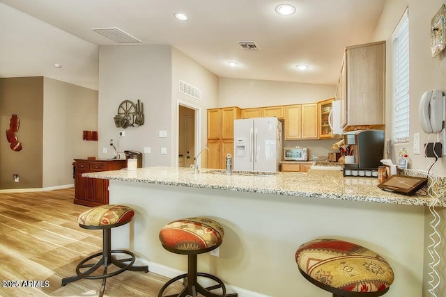 kitchen featuring vaulted ceiling, light brown cabinetry, light stone counters, kitchen peninsula, and white appliances