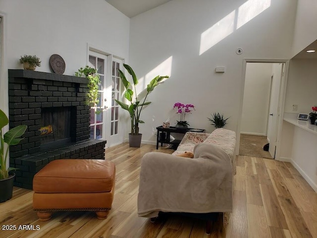 living room featuring a brick fireplace, a towering ceiling, and light wood-type flooring