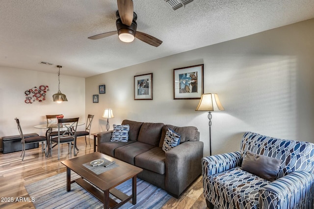 living room featuring wood-type flooring, a textured ceiling, and ceiling fan