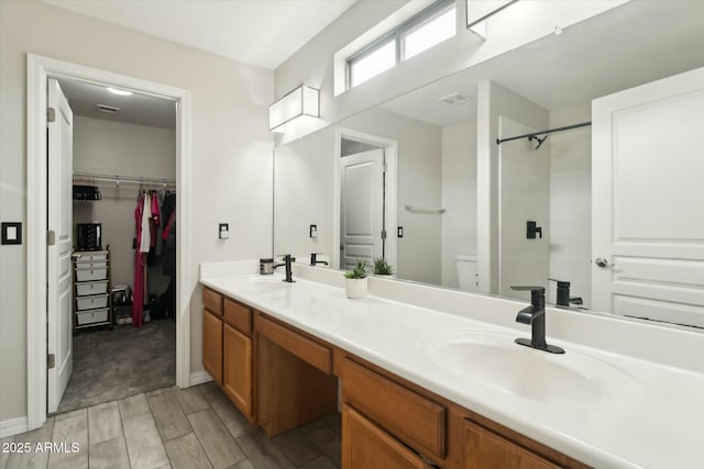 bathroom featuring visible vents, double vanity, a sink, and a walk in closet